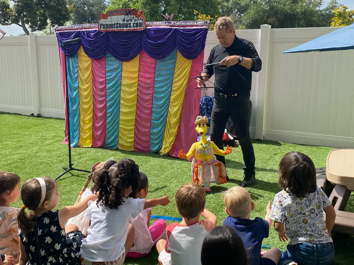 Children attending an outdoor performance with a guest entertainer during summer at Newport Ave Preschool